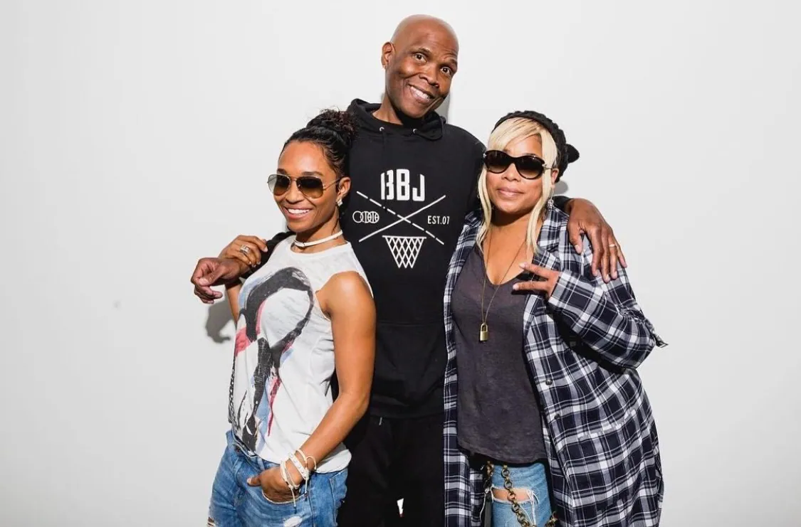 Three people against a white backdrop: a radio host in a BBJ crest tee with an arm around each of the two singers beside him.