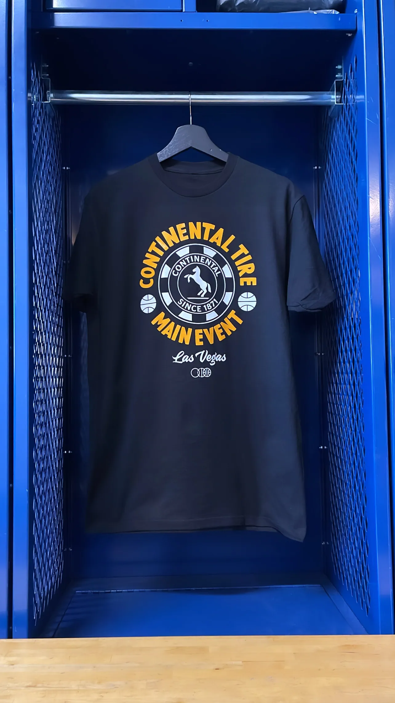 A navy tee on a hanger inside a lit blue locker, printed at the chest with a CONTINENTAL TIRE MAIN EVENT · LAS VEGAS roundel over the BBJ mark.