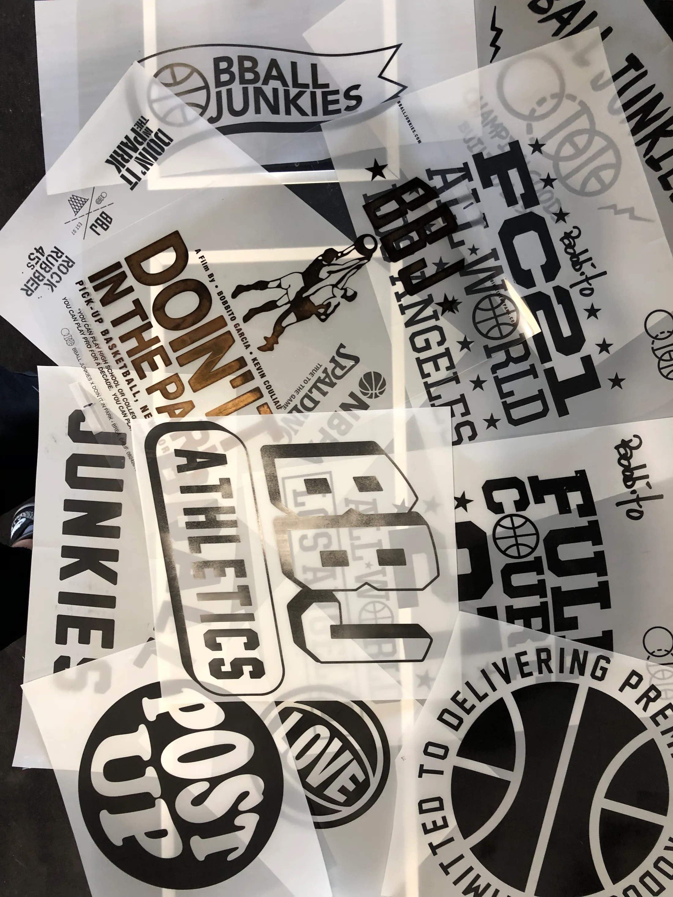 A spread of overlapping film positives on a light table — tournament lockups, wordmarks and roundels drawn for a dozen different jobs, black artwork on clear sheets.