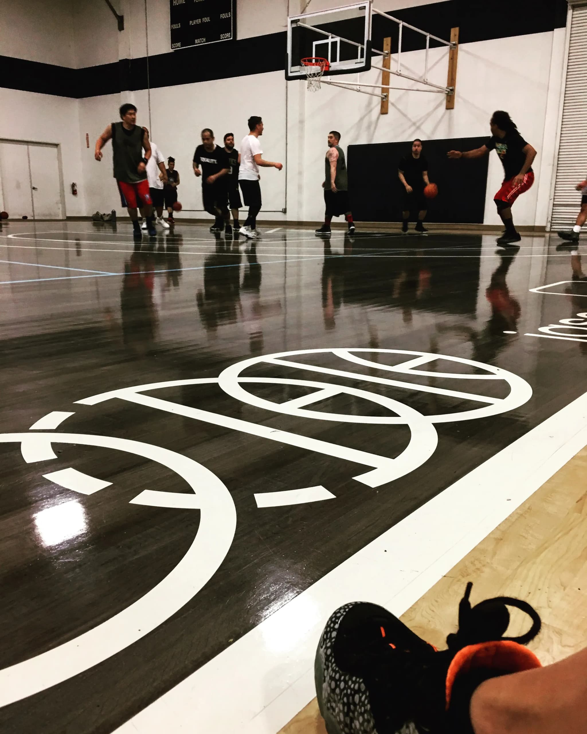 The BBJ three-ring icon painted the width of the key on a dark gym floor, a pick-up run going on beyond it under the backboard.