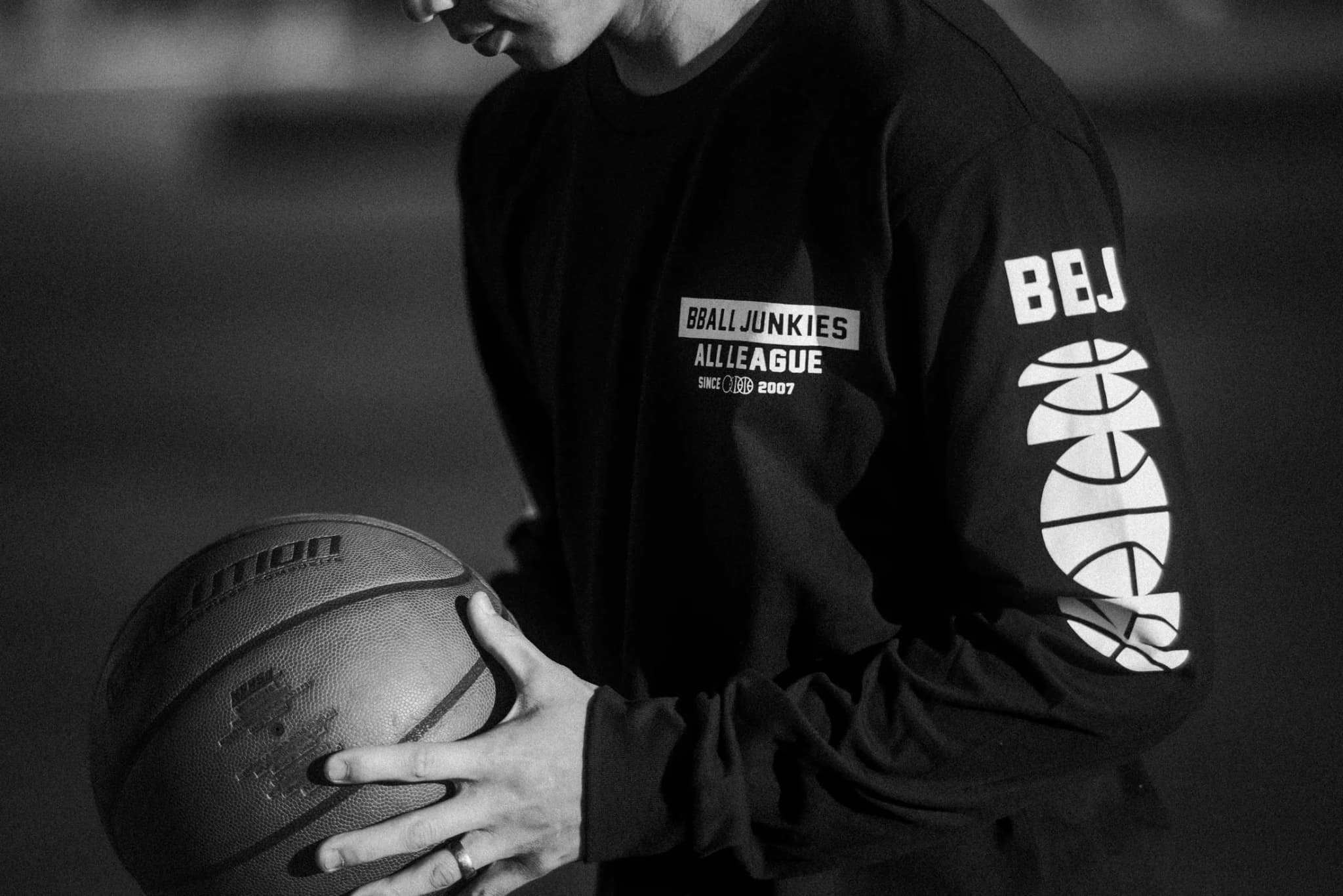 A close crop of the black BBALL JUNKIES All League long sleeve — chest label and sleeve print — a leather ball cradled in both hands.