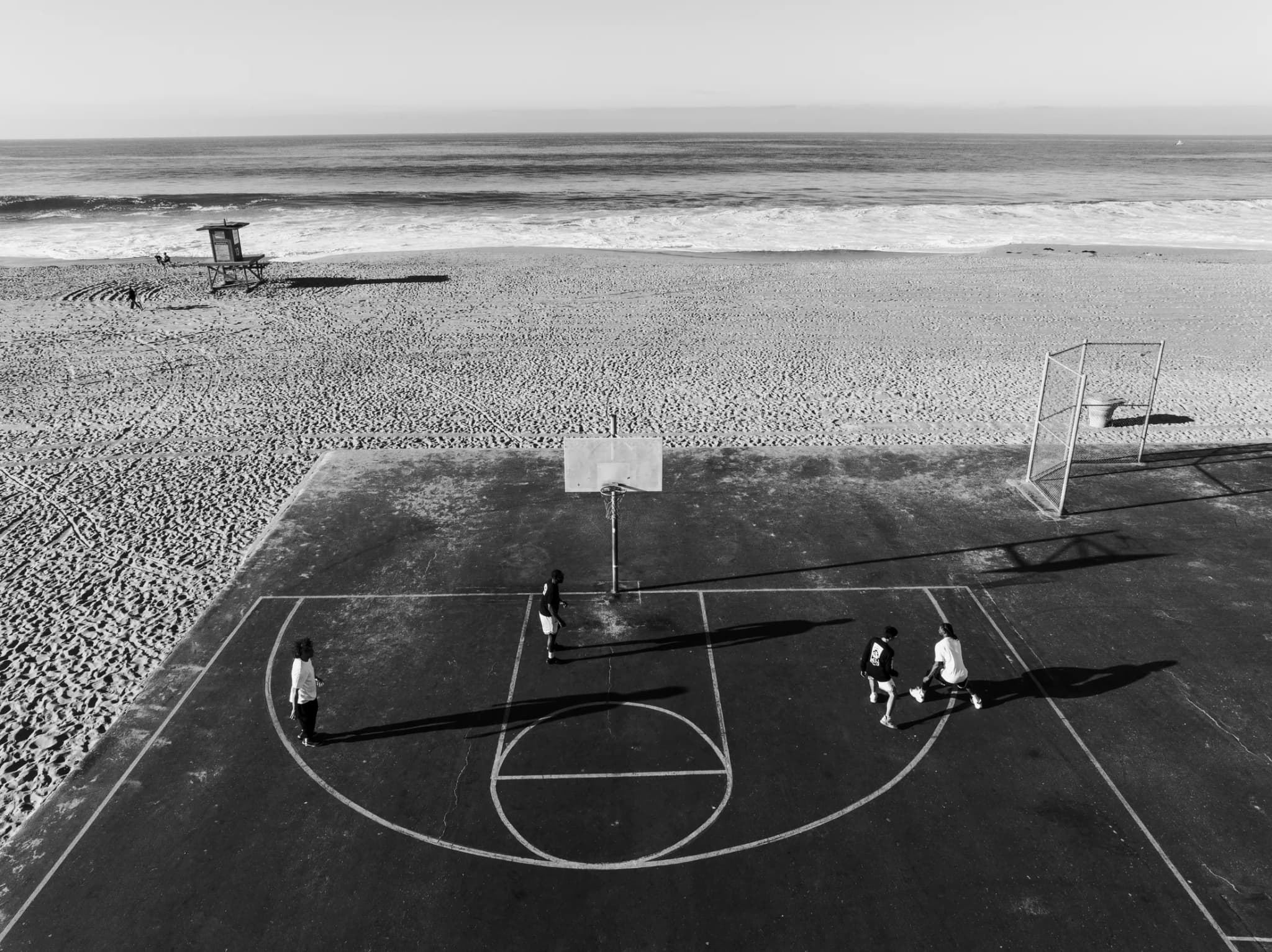 A beachside court seen from above, four players spread across the key, the sand and the surf beyond it.
