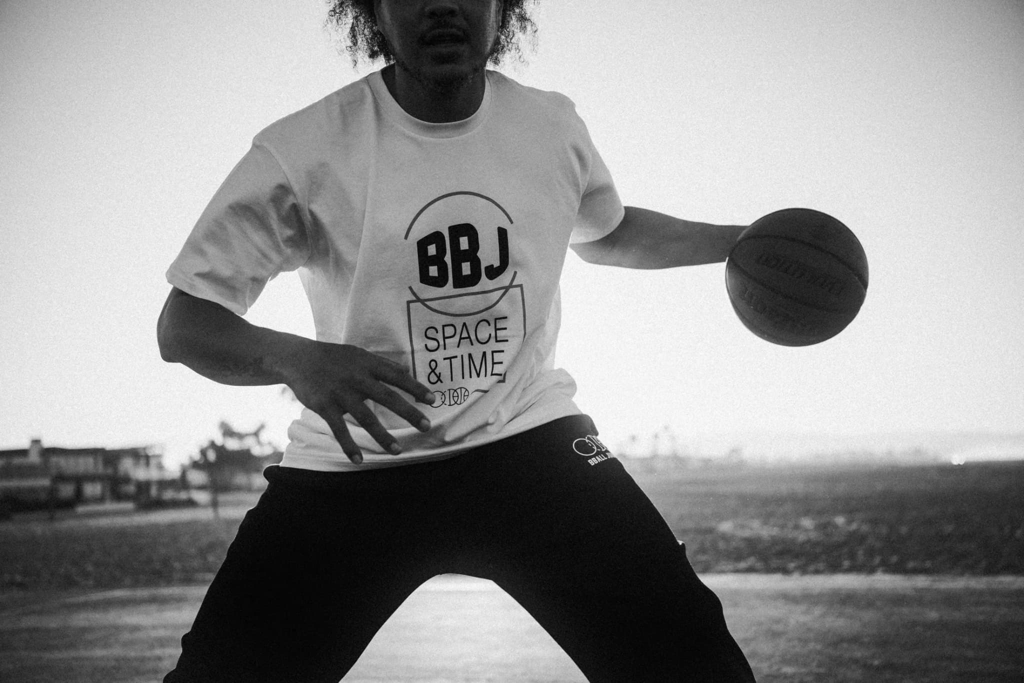A close crop of a player in the BBJ Space & Time tee working the ball at his hip against a low sun, beach houses along the horizon.