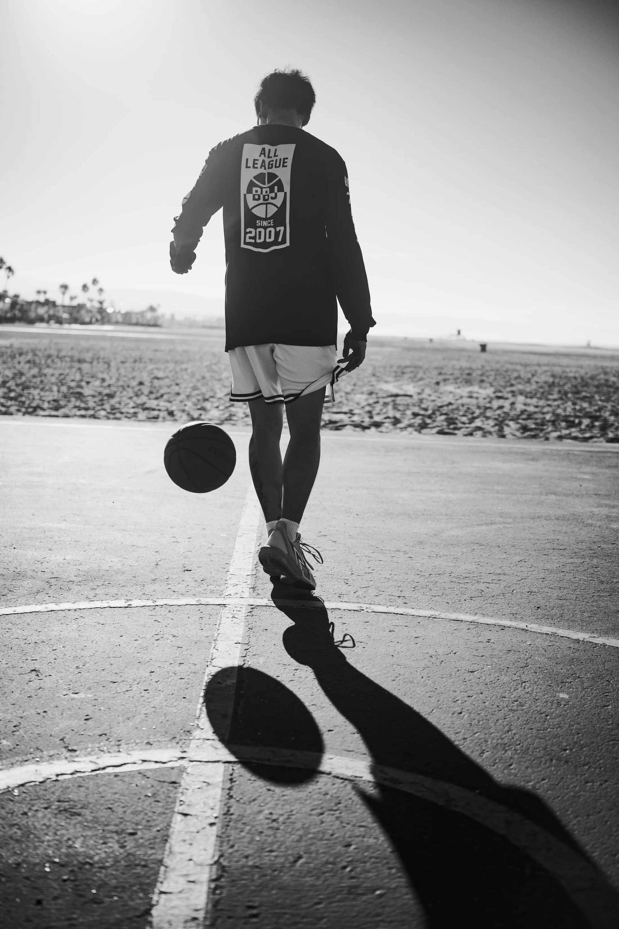A player seen from behind at the free-throw line, the All League crest on his back, the ball bouncing beside his shadow.
