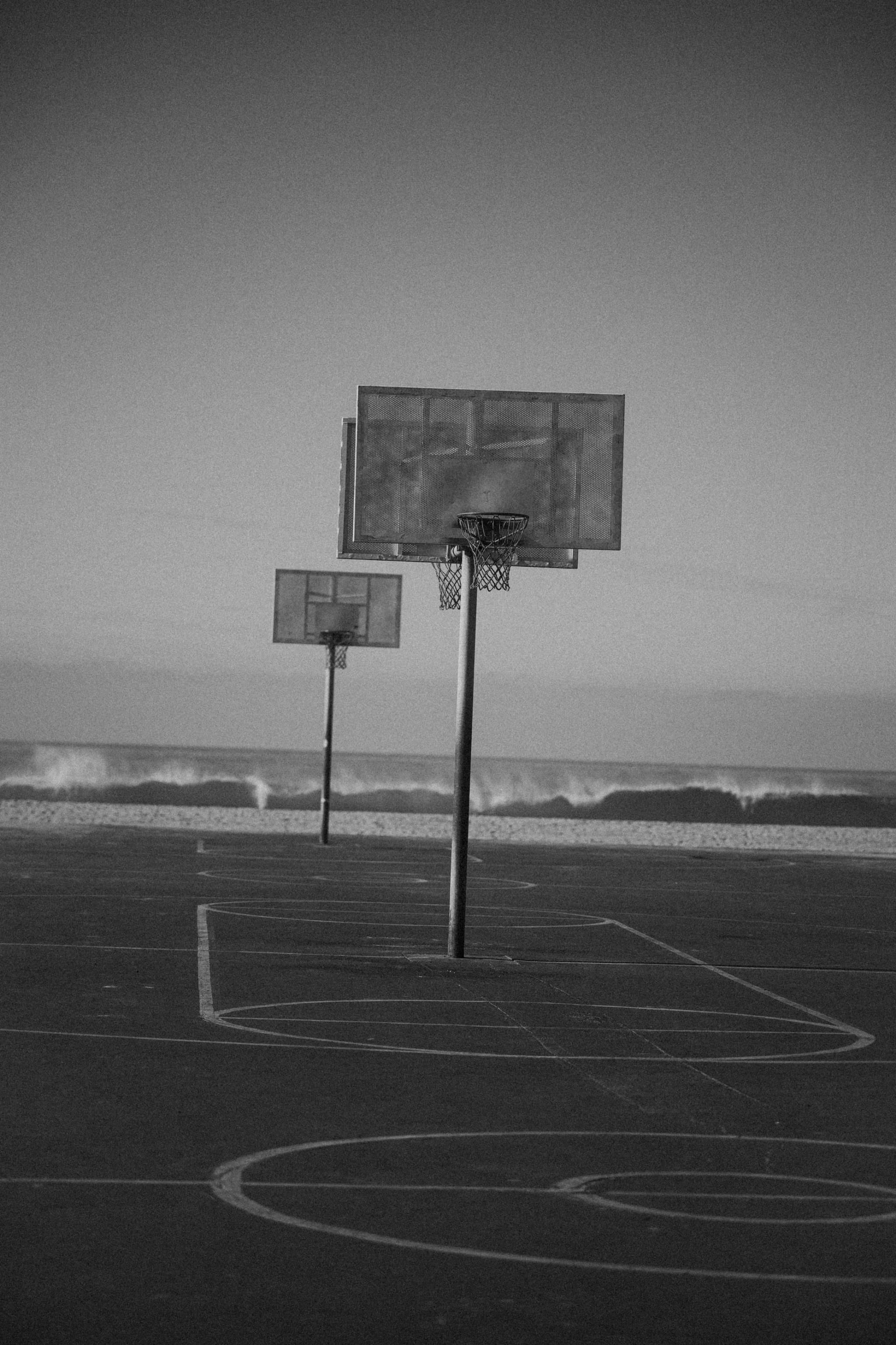 Two beachside hoops standing over an empty painted court, the surf breaking beyond.