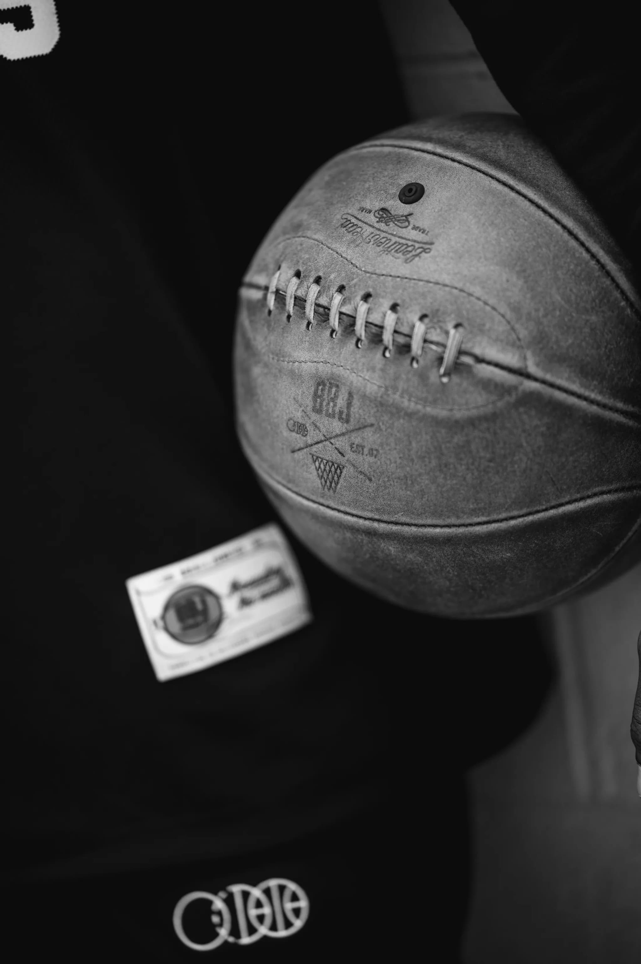 A leather BBJ basketball — the crest and Est. 07 stamped into the panel — held against a black jersey.