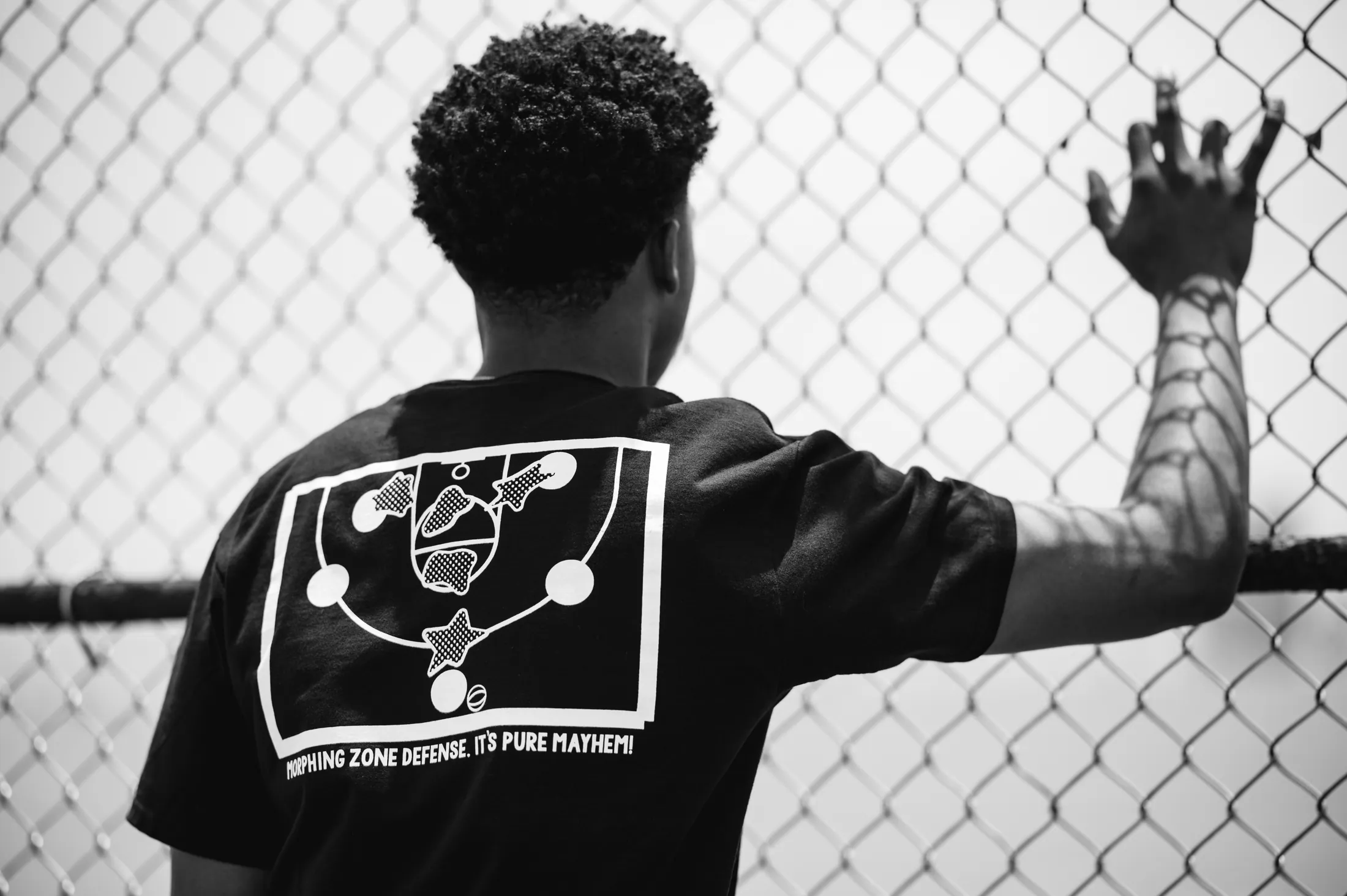 The back of the Morphing Zone Defense tee at a chain-link fence — a zone-defense play drawn across the shoulders.