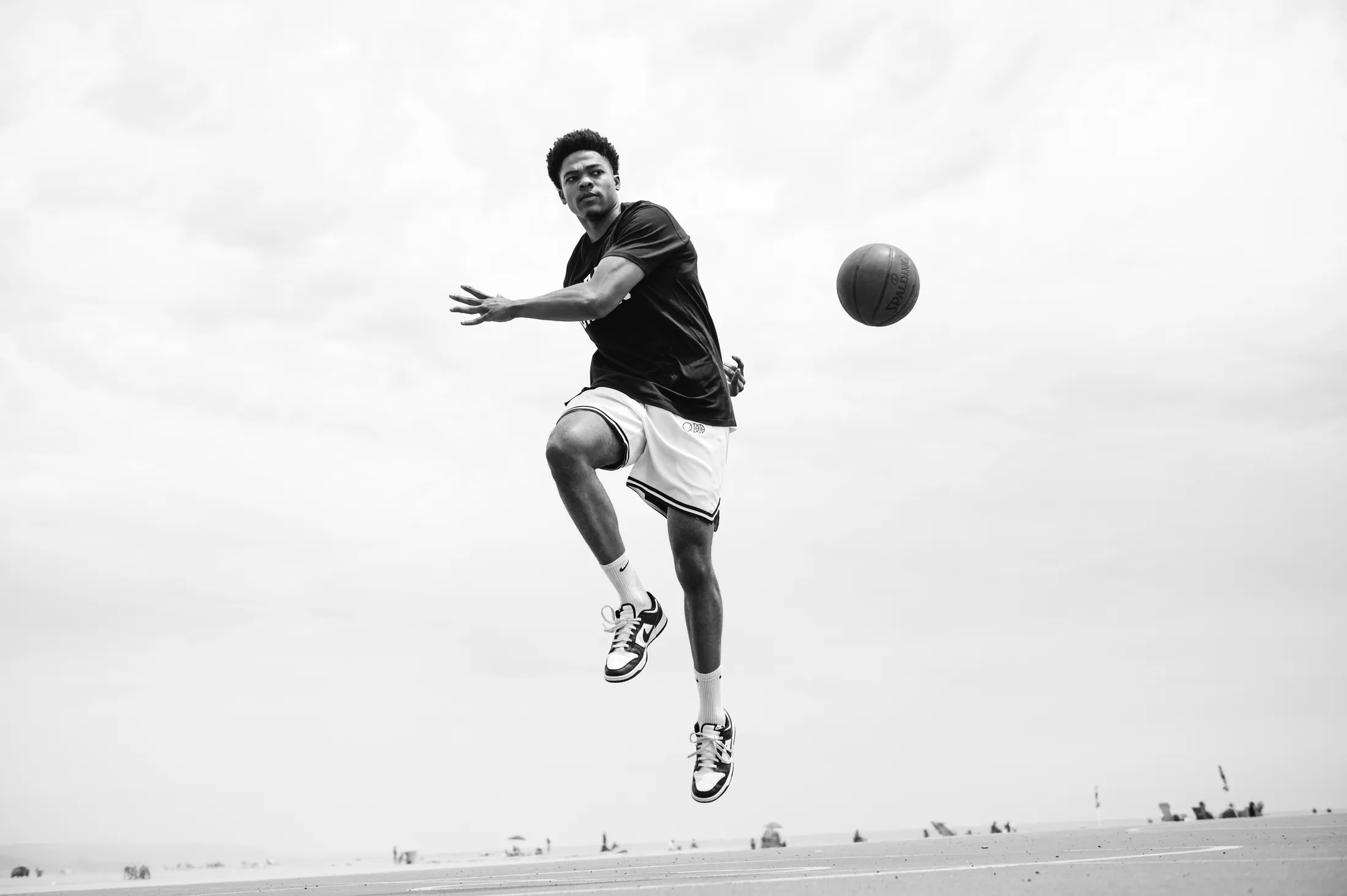 A player mid-air reaching for a loose ball, in a black BBJ tee and white BBJ shorts.