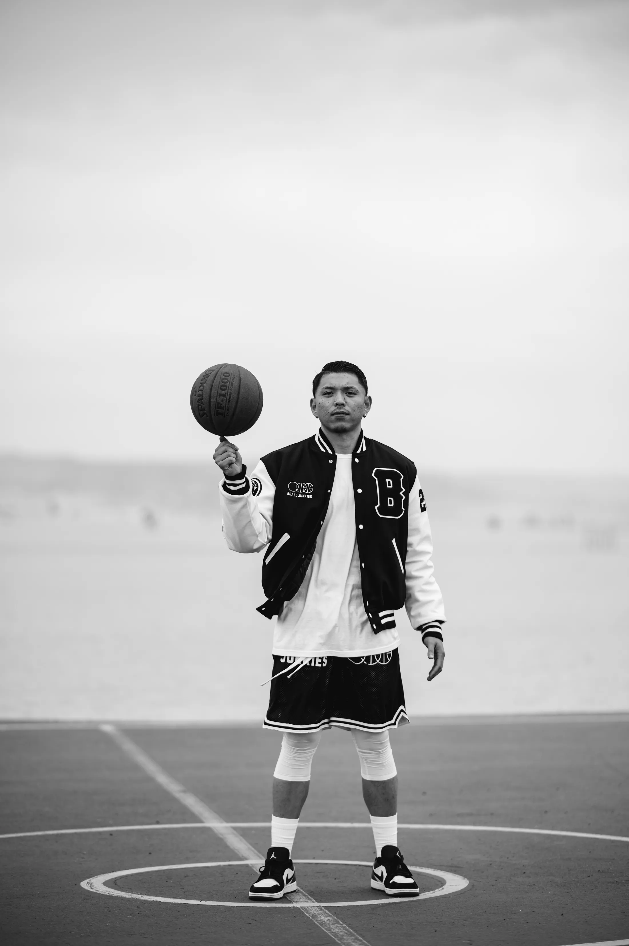 A player spinning a ball on one finger at the center circle of an outdoor court, in the BBJ varsity jacket.