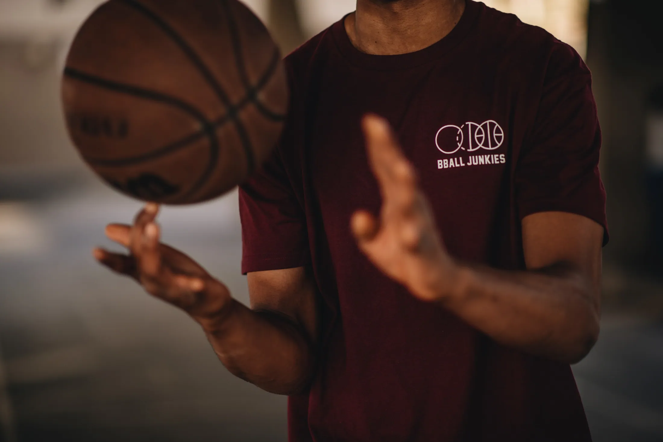 A ball spun up off one finger, the thrower in a burgundy tee carrying the BBJ three-ball mark at the chest.
