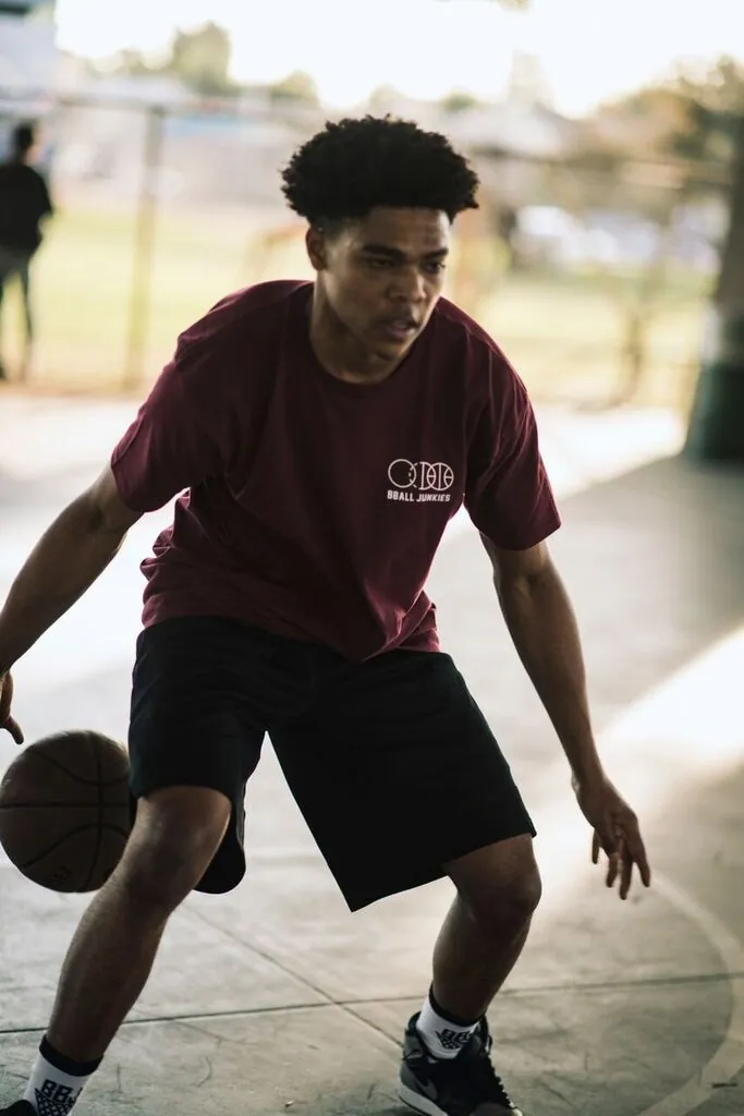 A player working the ball low on an outdoor court, in a burgundy BBJ tee and black shorts.
