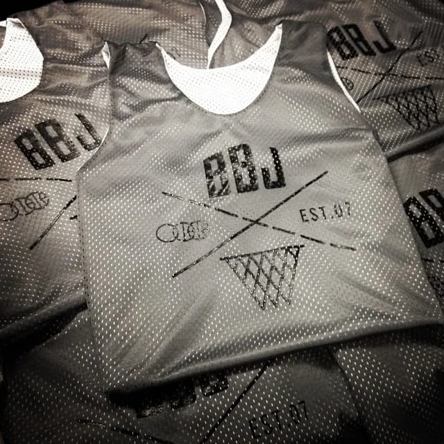 A stack of gray mesh reversible practice jerseys, each screen printed with the BBJ crossed-line and net mark over EST. 07, one folded flat on top.